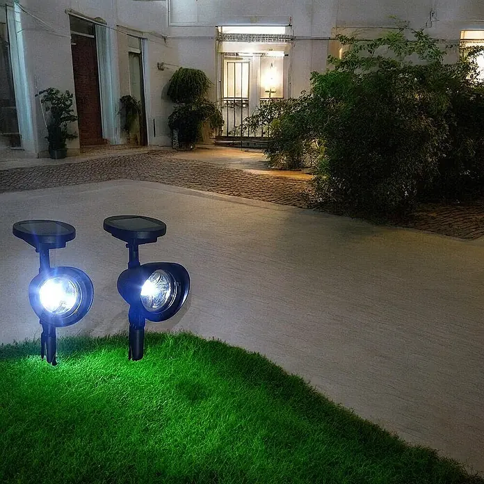 2 er Set LED Solarleuchten Solarstrahler -  - Zwei schwarze Solar-Bodenspots beleuchten nachts einen Gartenweg und Rasen.