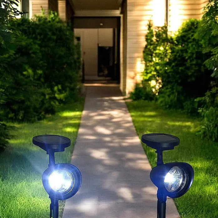 2 er Set LED Solarleuchten Solarstrahler -  - Zwei schwarze Solar-Bodenspots beleuchten nachts einen Weg zu einem Haus.