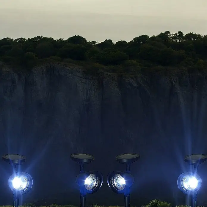 2 er Set LED Solarleuchten Solarstrahler -  - Vier blaue solarbetriebene Gartenspots mit integrierten Panelen beleuchten hell eine dunkle Außenlandschaft.