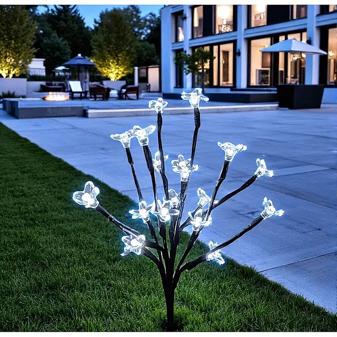 LED Solar Stick Flower klar 20 flg. -  - Ein künstlicher schwarzer Baum mit klaren, blütenförmigen LED-Leuchten strahlt nachts auf einem Rasen und beleuchtet eine Außenterrasse.