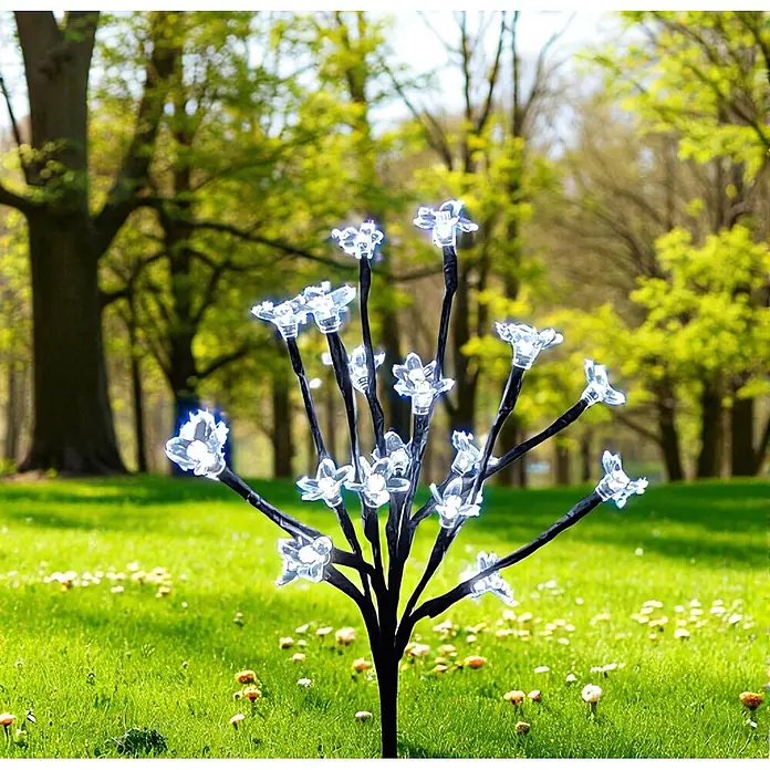 LED Solar Stick Flower klar 20 flg. -  - Dekorative schwarze LED-Baumleuchte mit klaren, blumenförmigen Lichtern in einer grünen Parklandschaft.