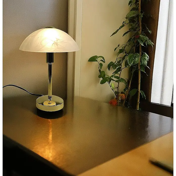 Tischleuchte Mischa Messing E14 -  - Halbkugelförmige Tischlampe mit weißem gemustertem Glasschirm und Chromfuß, beleuchtet einen dunklen Tisch.