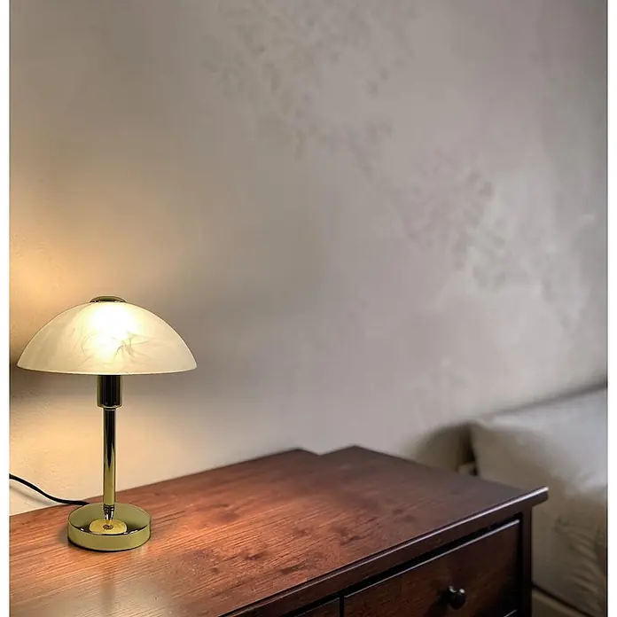Tischleuchte Mischa Messing E14 -  - Eine klassische Schreibtischlampe mit weißem Glasdomschirm und goldenem Fuß auf einem dunklen Holznachttisch.