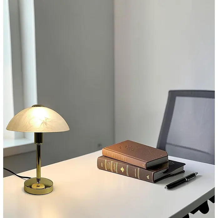Tischleuchte Mischa Messing E14 -  - Messingtischlampe mit mattiertem Kuppelschirm auf einem Schreibtisch mit Büchern und einem Stift.