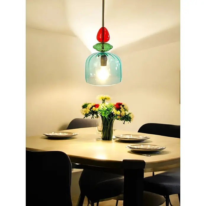 Pendelleuchte PIA einflammig Glasschirm -  - Bunte Glas-Pendelleuchte in Rot, Grün und Türkis, die einen Esstisch mit Blumenarrangement beleuchtet.