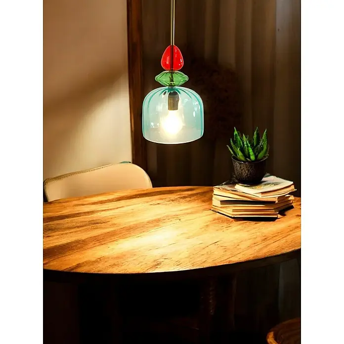 Pendelleuchte PIA einflammig Glasschirm -  - Eine farbige Glas-Pendelleuchte mit geriffelter blauer Schirm, grünen und roten Perlen, hängt beleuchtet über einem Holztisch.