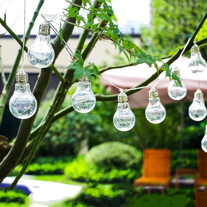 Solar-Lichterkette Glühbirne 10 flammig -  - Dekorative Lichterkette mit Glühbirnen aus Klarglas hängt an Ästen in einem Garten.