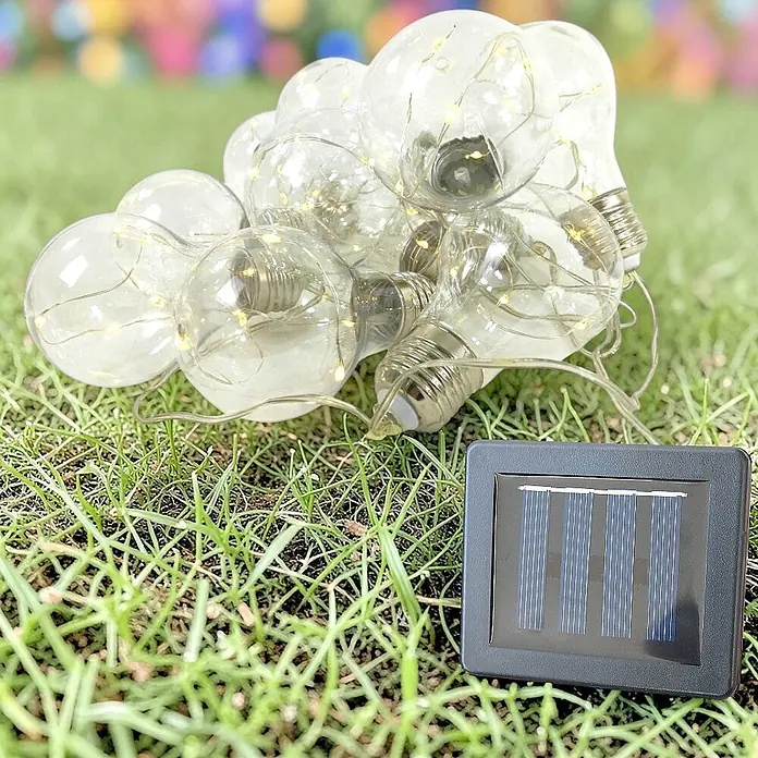 Solar-Lichterkette Glühbirne 10 flammig -  - Solarbetriebene Lichterkette mit klaren Glühbirnengehäusen und LEDs, neben einem schwarzen Solarpanel.
