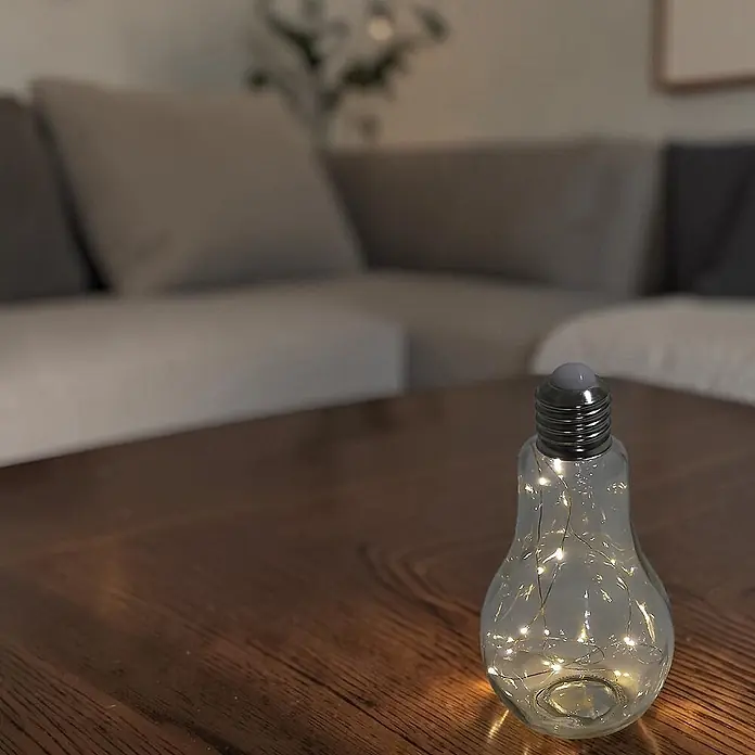 Dekoleuchte Tischlampe Glühbirne mit Lichterkette 20 LED batteriebetrieben -  - Eine glühbirnenförmige Glaslampe mit warmen Lichterketten steht auf einem Holztisch. Sie spendet Umgebungslicht im Wohnzimmer.