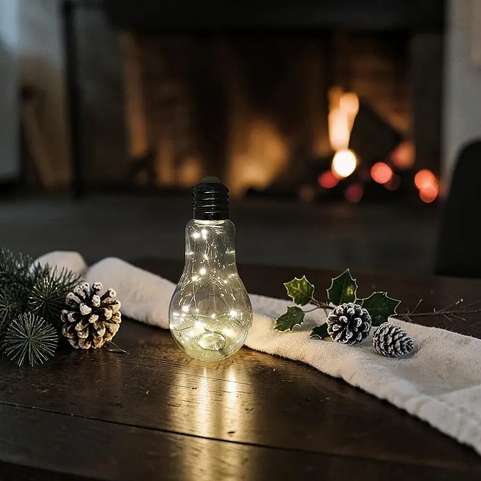 Dekoleuchte Tischlampe Glühbirne mit Lichterkette 20 LED batteriebetrieben -  - Eine klare, birnenförmige Dekolampe mit warmen Lichterketten steht auf einem Holztisch, umgeben von festlichem Grün.
