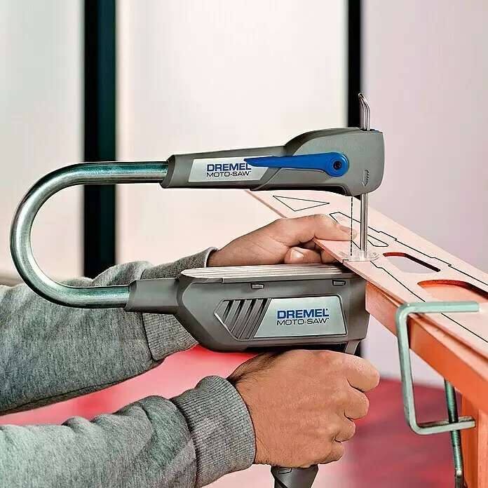 Dremel Moto-Saw Sierra de marquetería MS20-1/5 - 70 W, Longitud hoja de sierra: 10,5 cm - Una persona utiliza una Dremel Moto-Saw gris y azul para cortar formas intrincadas en un trozo de madera clara sujeto a un banco de trabajo.