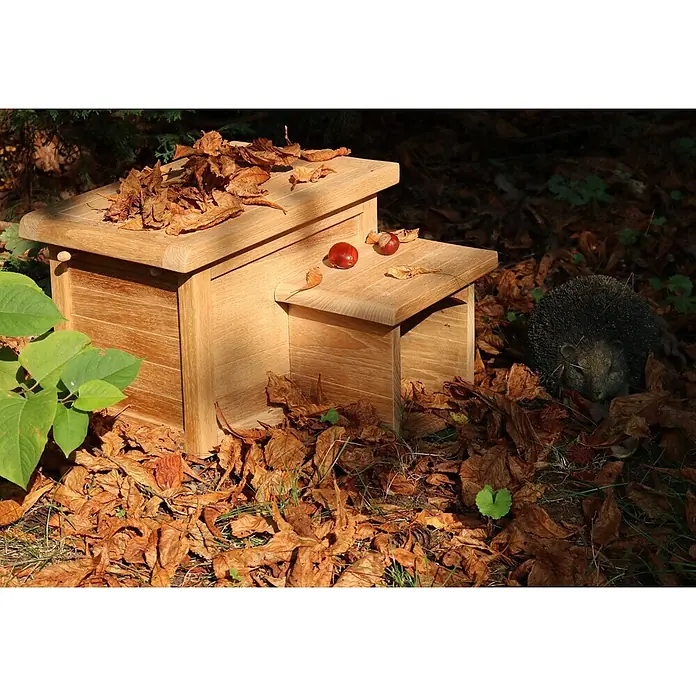 Teak Igelhaus Friesenlaub als Igelhotel 36 x 45 cm Massivholz montiert -  - Helles Holz-Igelhaus inmitten von Herbstlaub, mit einem Igel daneben.