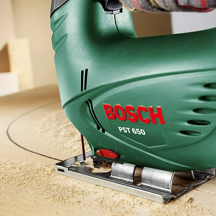 Bosch Elektro-Stichsäge PST 650 - 3.100 /min, 65 mm - Nahaufnahme einer grünen Bosch PST 650 Stichsäge beim Schneiden eines Kreises in ein Holzbrett.