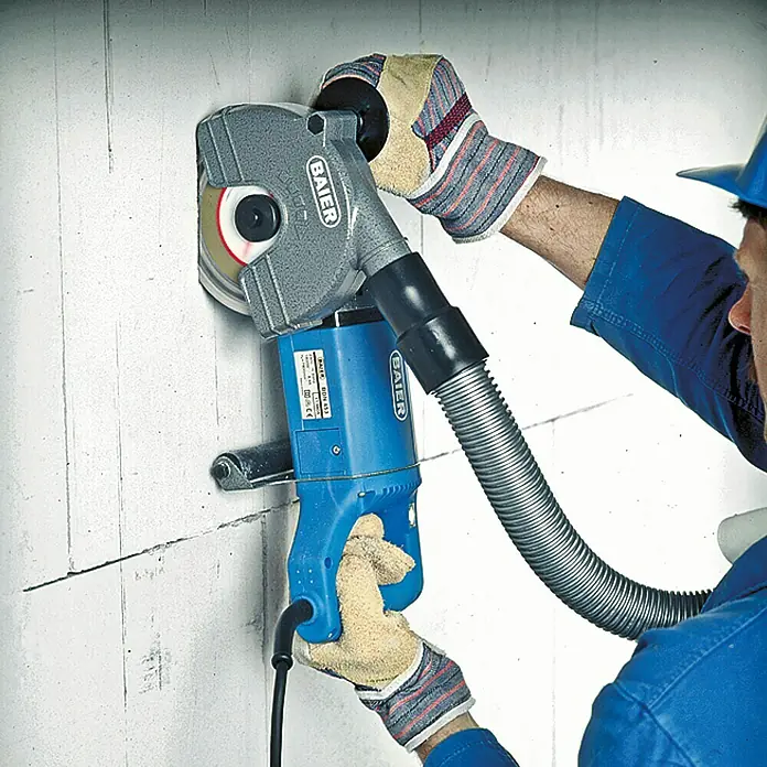 Baier Mauernutfräse BDN 452 - 150 mm - Eine Mauernutfräse von Baier im Einsatz, bedient von einer Person in Arbeitskleidung und Handschuhen. Das Werkzeug schneidet präzise Nuten in eine Wand.