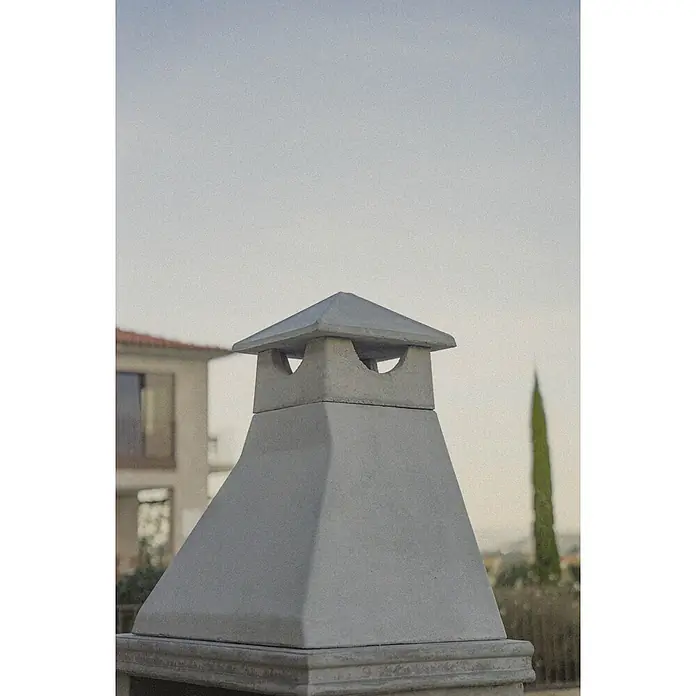 Sotnas Barbacoa de obra Ibiza - Gris/Ladrillo, An x Pr x Al: 168 x 60 x 219 cm, Superficie parrilla: 60 x 38 cm, Con fregadero - Un remate de chimenea cuadrado de hormigón gris con cuatro aberturas arqueadas, visto al aire libre con una casa y un ciprés difuminados.