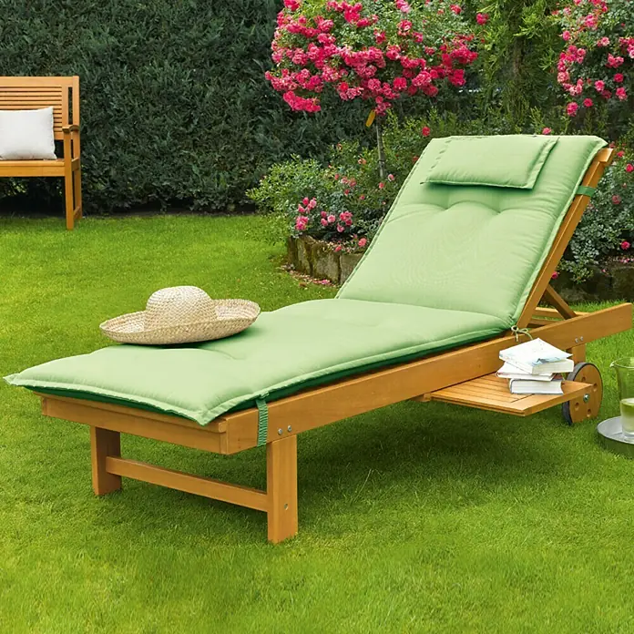 Sunfun Diana Tumbona de jardín - 65 x 190 x 33 cm, Marrón natural, Madera, Barra antivuelco - Una tumbona de madera con un cojín verde en un jardín, al lado de una mesita con libros y una bebida.