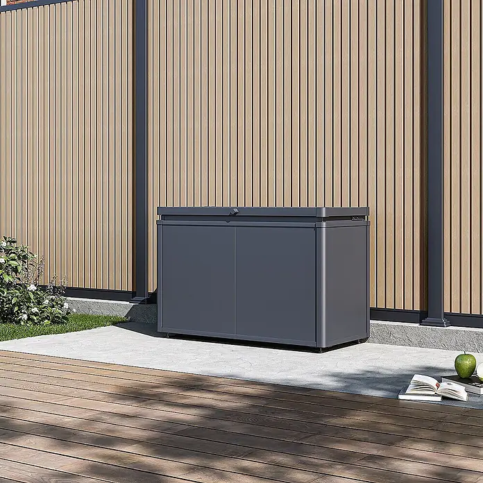 Weide Noble Gartenbox 290 L Stahl/Alu 1 m x 46 cm x H 64 cm Anthrazit -  - Dunkelgraue Outdoor-Aufbewahrungsbox auf einer Terrasse neben einem Holzzaun. Ideal für Gartenwerkzeuge oder Kissen.