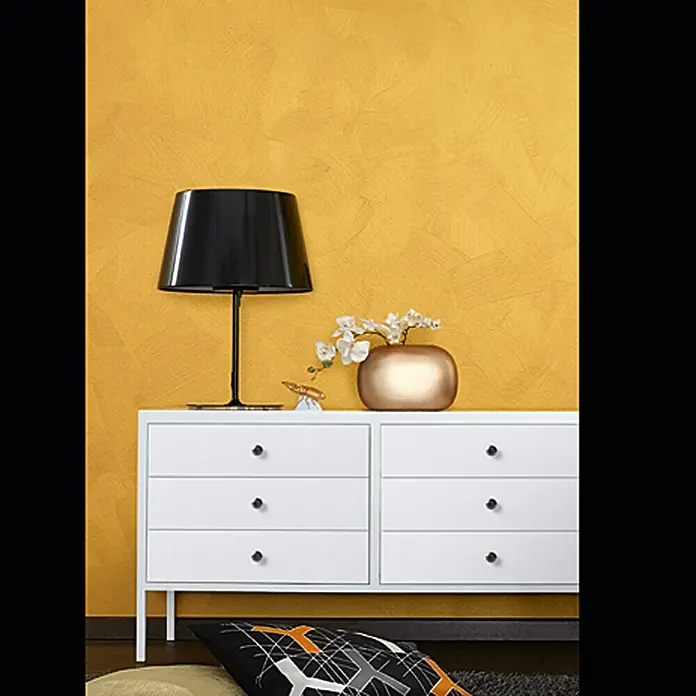 SCHÖNER WOHNEN-Farbe Trendstruktur Farbeffektputz Metall-Optik Effektfarbe - Mattgold, Matt, 2,5 l - Elegante weiße Kommode mit einer stilvollen Lampe und dekorativer Blumenvase auf gelbem Hintergrund.