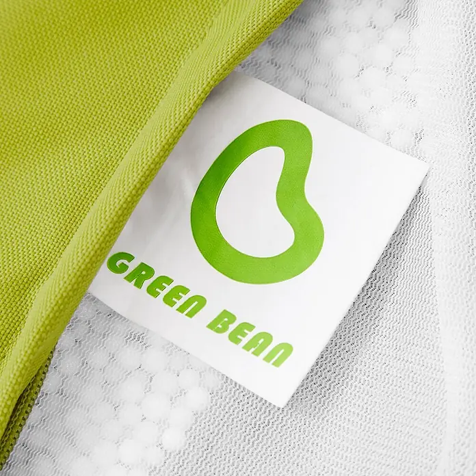 Green Bean Sitzhocker Cube mit EPS Füllung 40x40x40 cm Grün -  - Weißes Produktetikett mit grünem Bohnen-Logo und "GREEN BEAN" Schriftzug, an hellgrünem Stoff und weißem Netz befestigt.