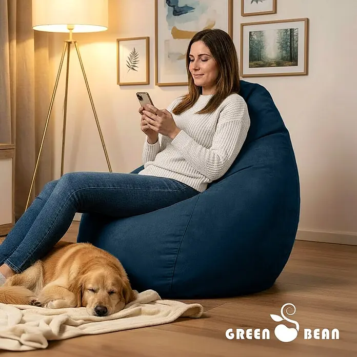 Green Bean Sitzsack Drop mit Rückenlehne 60x60x90 cm Dunkelblau -  - Blauer Sitzsack im Wohnzimmer, mit einer Frau, die bequem darauf sitzt und ihr Telefon benutzt, und einem schlafenden Hund daneben.