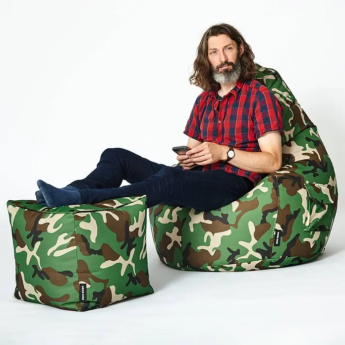 Green Bean Sitzhocker Cube mit EPS Füllung 40x40x40 cm Camouflage Grün -  - Ein Mann entspannt auf einem Camouflage-Sitzsack mit den Füßen auf einem passenden Hocker, ein Telefon haltend.
