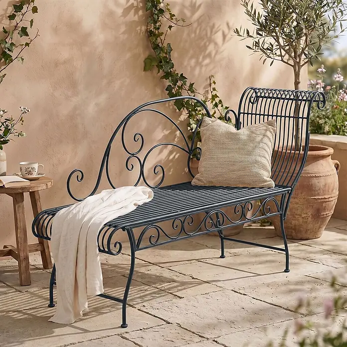 Furnicato Gartenbank Karma Recamiere aus Eisen im Jugendstil -  - Dunkelgraue Metall-Gartenliege mit Zierschnörkeln, einem Webkissen und einer Decke auf einer Terrasse.