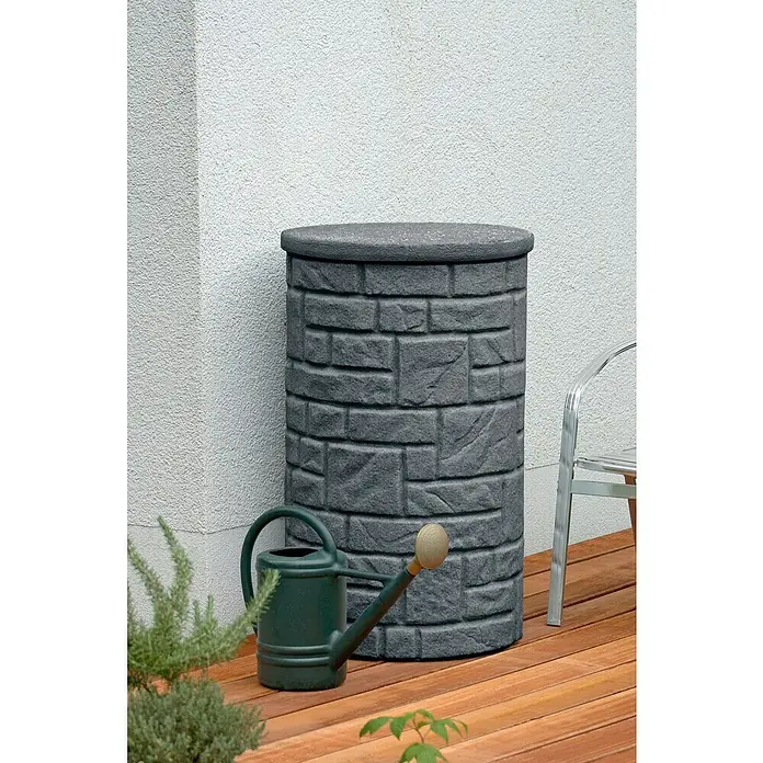 Arves Regenspeicher Arcado - 230 l, Black Granitfarben - Nahaufnahme einer stilvollen Regentonne in Steinoptik mit einer grünen Gießkanne auf einer hölzernen Terrasse vor einer hellen Wand.