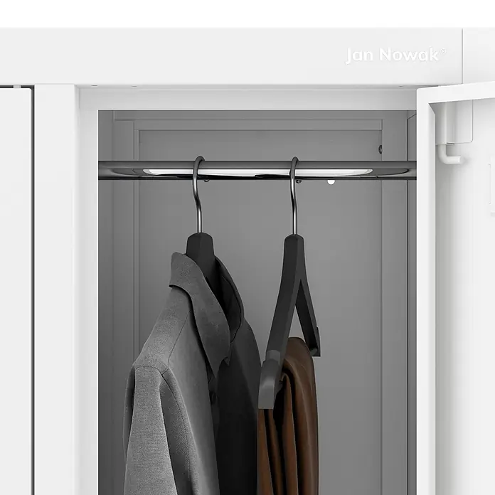 Jan Nowak Arbeitsschutzschrank BARTEK, 10-türig, 136x172x45 cm, Weiß -  - Im Inneren eines weißen Schranks hängen ein graues Hemd und eine braune Hose an schwarzen Kleiderbügeln an einer Metallstange.