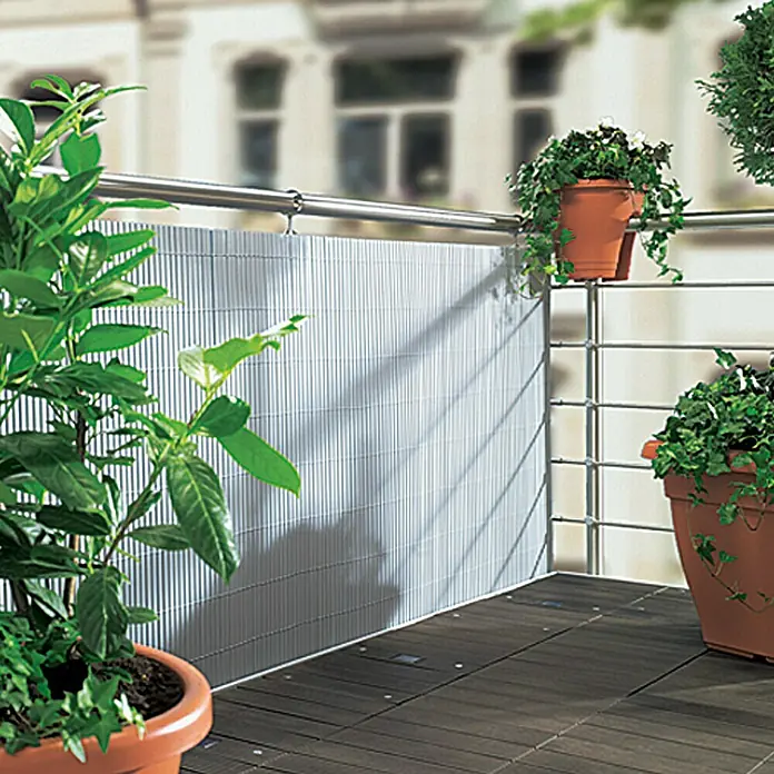 Gardol Comfort Sichtschutzmatte - Silber, 300 x 90 cm - Das Bild zeigt einen Balkon mit einem Sichtschutz aus grauen Lamellen, umgeben von üppigen Pflanzen in Terrakotta-Töpfen. Der Boden ist aus dunklem Holz gefertigt.