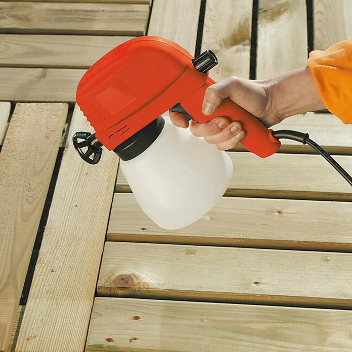 Lehnartz Elektrische Spritzpistole Easy-Sprayer PLUS - 45 W - Eine Nahaufnahme einer Person, die einen roten Farbsprüher verwendet, um ein Holzdeck zu streichen. Der Farbsprüher ist das Hauptprodukt im Fokus.