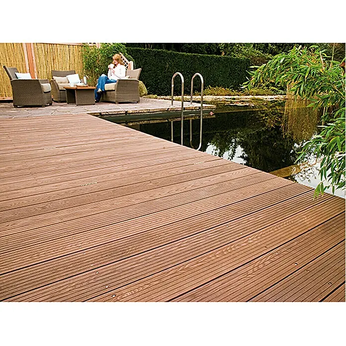 Osmo Bangkirai-Öl 006 - Naturgetönt, Transparent, 750 ml, Seidenmatt - Eine Terrassendiele aus braunem Holz führt zu einem Teich mit einer Leiter und einer Sitzgruppe mit einer Person im Hintergrund.
