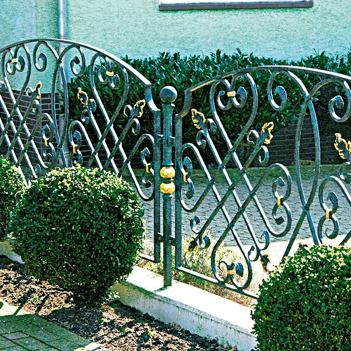 Hammerite Metall-Schutzlack - Schwarz, 400 ml, Glänzend, Lösemittelbasiert - Eine dekorative Gartenzaun aus Metall mit kunstvollen Verzierungen und goldenen Akzenten vor üppigem Grün.