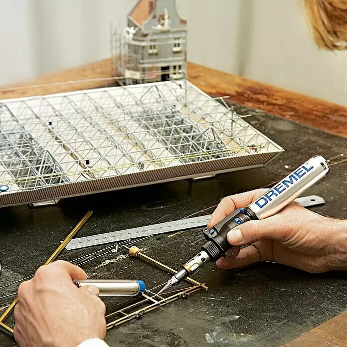Dremel VersaTip Soldador a gas 2000-6 - Largo: 19 cm - Manos usan una multiherramienta Dremel plateada y negra para soldar pequeñas piezas metálicas de un modelo.