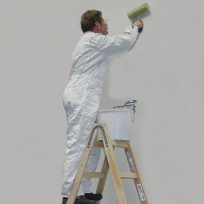 Krause Stabilo Escalera doble - Número de peldaños: 10 ud., Altura de trabajo: 2,75 m, Carga soportada: 150 kg, Madera - Hombre con mono blanco pintando una pared con rodillo mientras está en una escalera de madera.