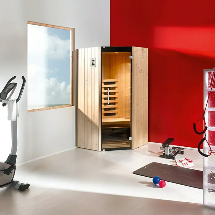 Weka Infrarotkabine Tanilla Eck - 1.400 W, 4 Keramikstrahler, 99 x 99 x 190 cm - Bild einer Sauna aus hellem Holz in einem hellen Raum mit Sportgeräten. Die Sauna ist das Hauptprodukt.