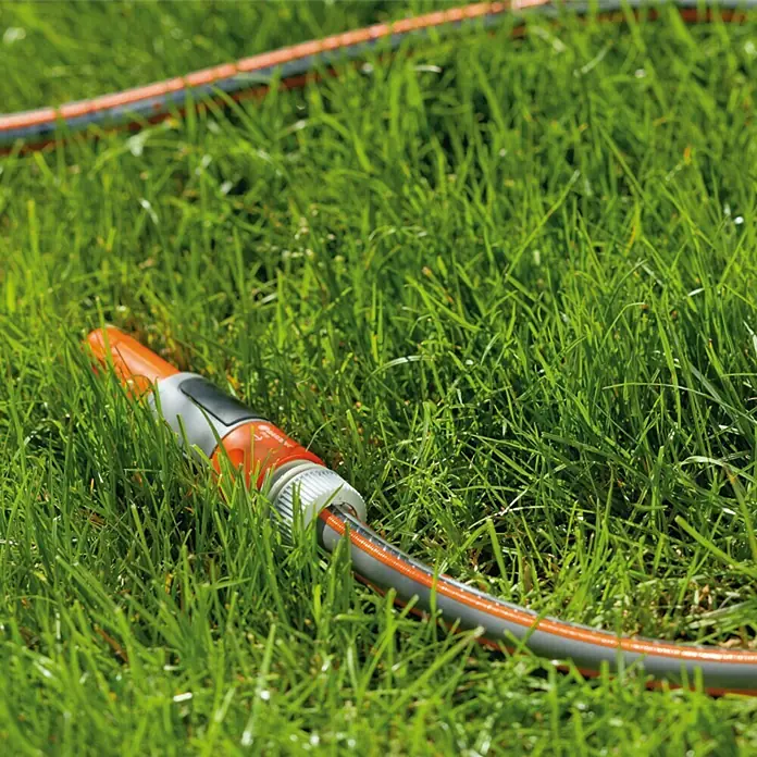 Gardena Schlauch Comfort High Flex - Länge: 50 m, Schlauchdurchmesser: 19 mm - Gartenschlauch mit orangefarbenem Sprühkopf liegt im grünen Gras. Bewässerung im Garten mit einem flexiblen Wasserschlauch.