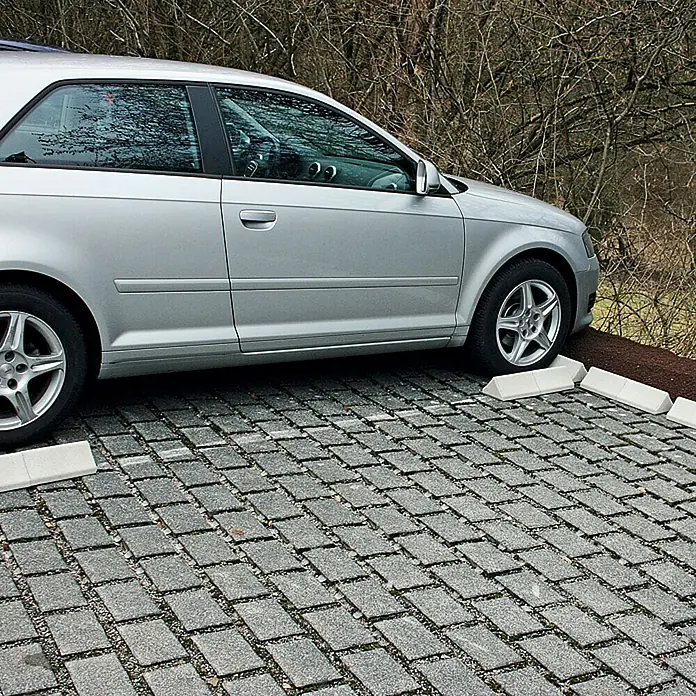Christoph Auto-Stop - Weiß, 25 x 14,8 x 10 cm, Beton - Silbernes Auto parkt auf einem Parkplatz mit grauen Pflastersteinen und weißen Radstopps.