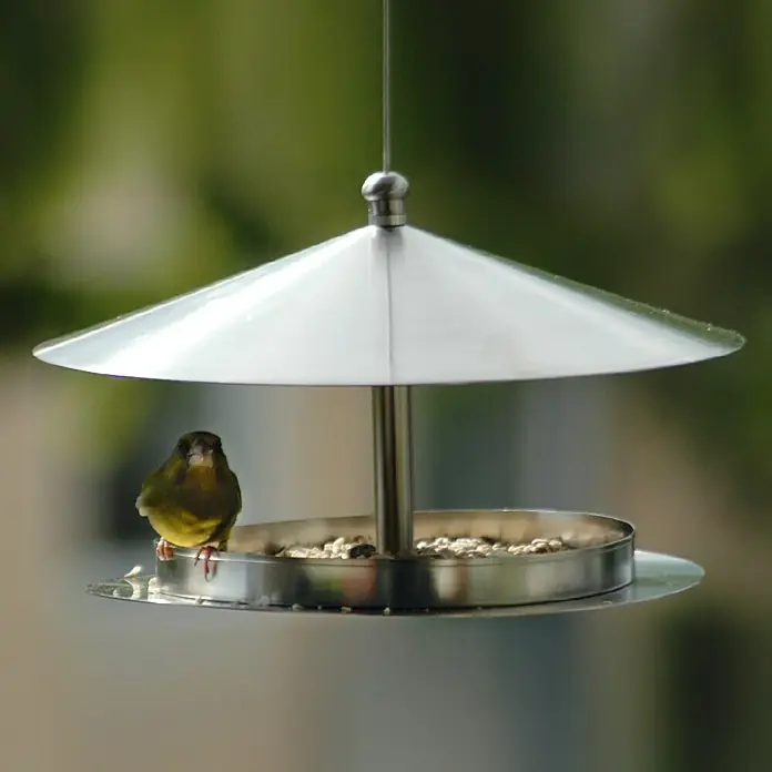 Dobar Vogelhaus Silberglanz - Durchmesser: 29 cm, Höhe: 19,5 cm, Silber, Edelstahl - Ein kleiner Vogel sitzt auf einem eleganten, silbernen Vogelfutterhaus, das mit Vogelfutter gefüllt ist und von einem schützenden Dach beschattet wird.