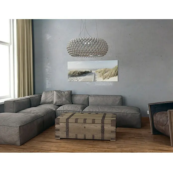ProArt Maritime Glasbild - Seeblick III, B x H: 125 x 50 cm - Ein stilvolles Wohnzimmer mit einem grauen Sofa, einem dekorativen Couchtisch und einer auffälligen Kristall-Hängeleuchte.