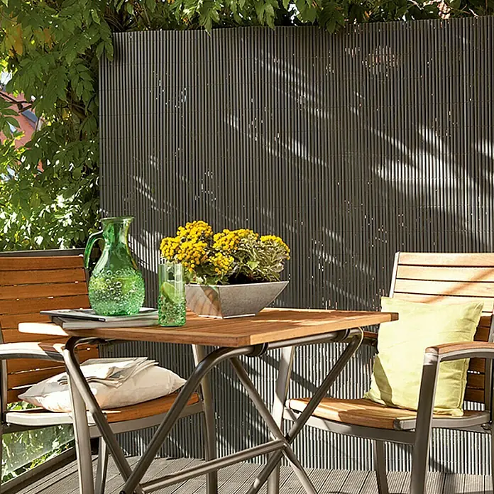 Gardol Comfort Sichtschutzmatte - Anthrazit, 300 x 90 cm - Ein gemütlicher Gartentisch mit Stühlen, dekoriert mit Blumen und einer grünen Karaffe, ideal für entspannte Stunden im Freien.