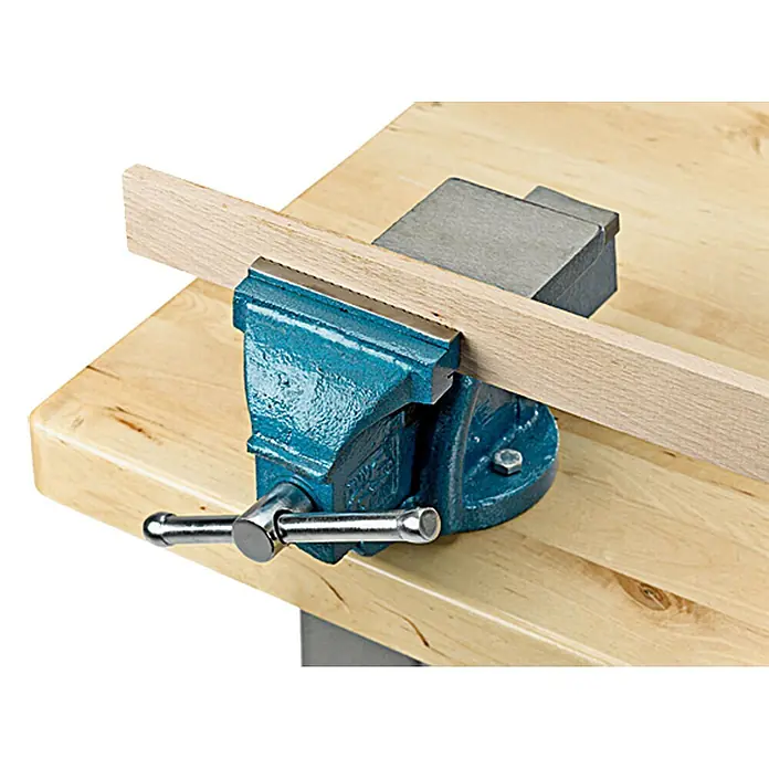 Tornillo de banco - 125 mm, Fijo, Metal - Torno de banco sobre una mesa de trabajo sujetando un trozo de madera. Ideal para asegurar piezas en varias tareas.