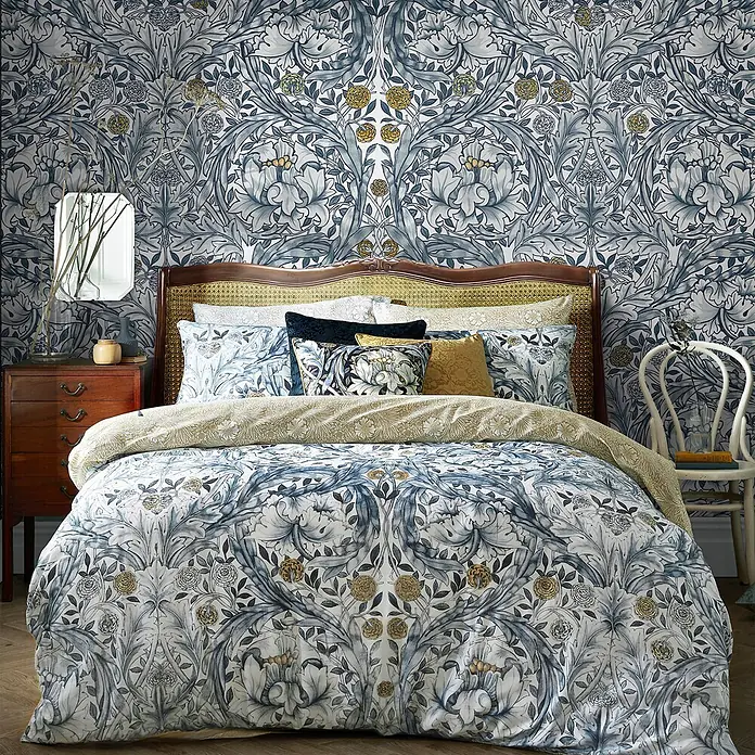 William Morris At Home Fototapete African Marigold - Blau - Schlafzimmer mit einem Bett, das ein blau, gold und weiß gemustertes Bettwäscheset mit passender Tapete zeigt.