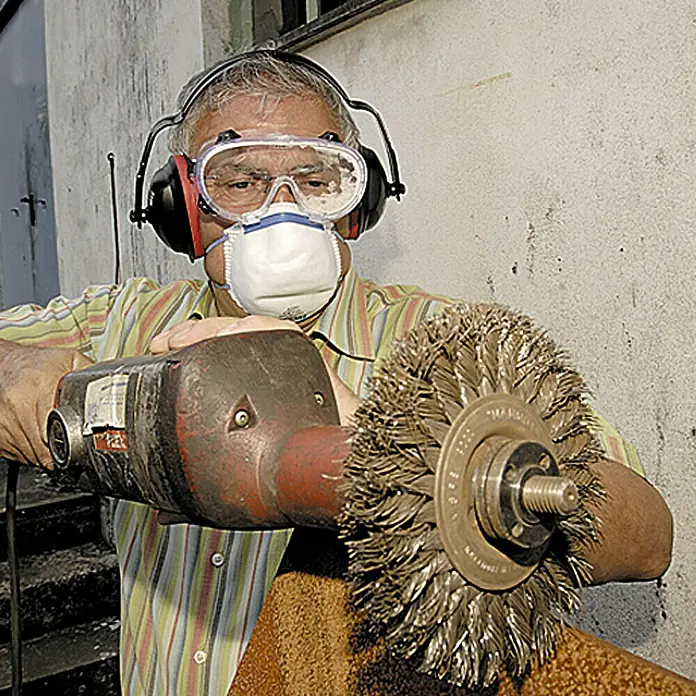 Wisent Auriculares de protección - Rojo/Negro - Un hombre usa un cepillo de alambre en una máquina mientras usa equipo de seguridad.