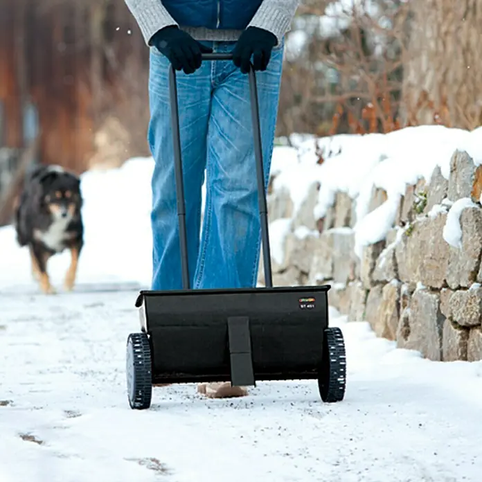 Gardol Carro esparcidor ST 451 - 12 l, Plástico - Persona empujando un esparcidor negro en un camino nevado, probablemente para deshielo.