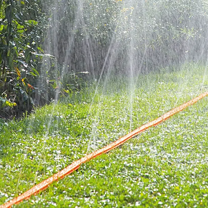 Gardena Schlauchregner - Länge: 15 m, Mit Wasserstopp - Rasensprenger im Einsatz. Der orangefarbene Sprinkler bewässert den grünen Rasen effektiv und sorgt für eine üppige Vegetation.