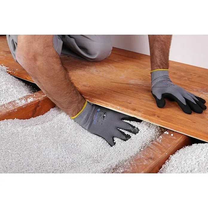 Knauf Isoself Hohlraumdämmung - 100 l - Ein Handwerker verlegt einen Bodenbelag mit isolierendem Füllmaterial. Die grauen Arbeitshandschuhe schützen die Hände bei der Installation.