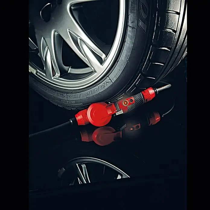 ABL Sursum Gummi-Schutzkontakt-Kupplung SCHUKOultra Pro - Rot/Schwarz, 250 V, IP54 - Ein roter Reifenfüller liegt auf einer glänzenden Oberfläche, neben einem Autoreifen. Das Gerät hat ein schlankes, modernes Design.