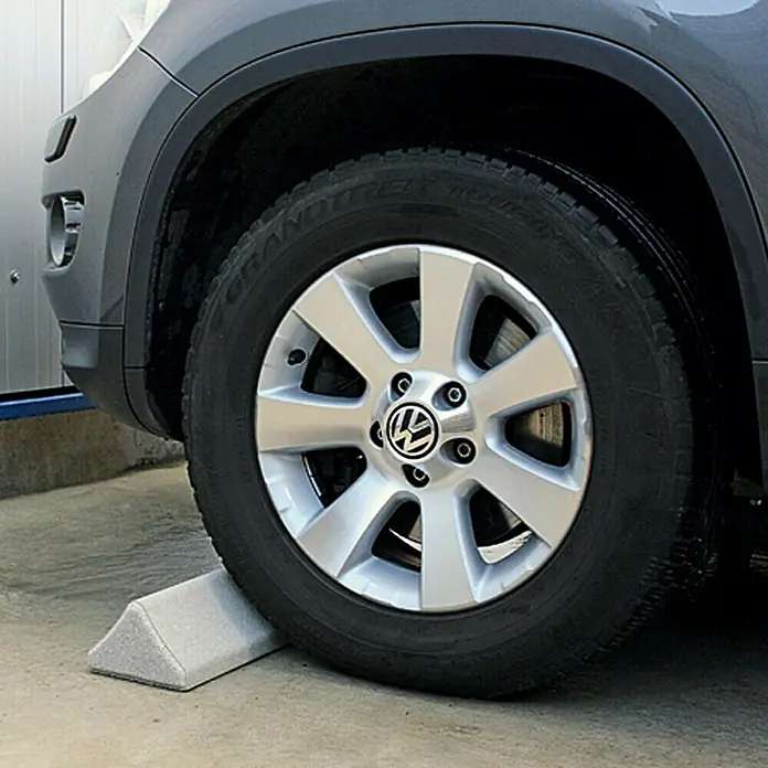 Christoph Auto-Stop - Weiß, 25 x 14,8 x 10 cm, Beton - Rad eines grauen VW Tiguan steht auf einem grauen Keil. Das Rad wird durch den Keil am Wegrollen gehindert.