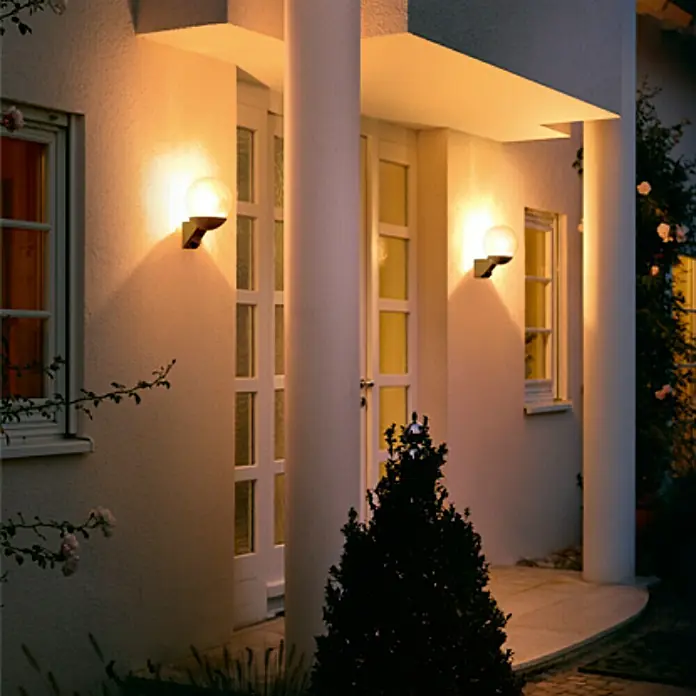 Steinel Aplique exterior con sensor L 585 - 60 W, 22,8 x 21,5 x 30,7 cm, Negro, IP44 - Una fachada de casa con dos luces redondas de exterior que emiten un brillo cálido, iluminando la zona de entrada.