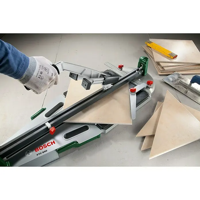 Bosch Fliesenschneider PTC 640 - Max. Schnittlänge: 640 mm - Bild einer Bosch PTC 640 Fliesenschneidmaschine in Aktion, demonstriert präzise Schnitte mit einer Hand und diversen Werkzeugen.